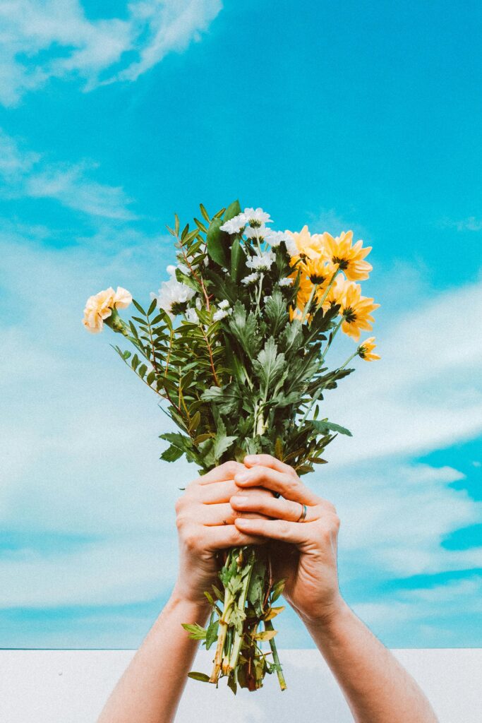 pexels photo 2106037 2106037 Hands holding a colorful flower bouquet beneath a vivid spring sky, symbolizing renewal.